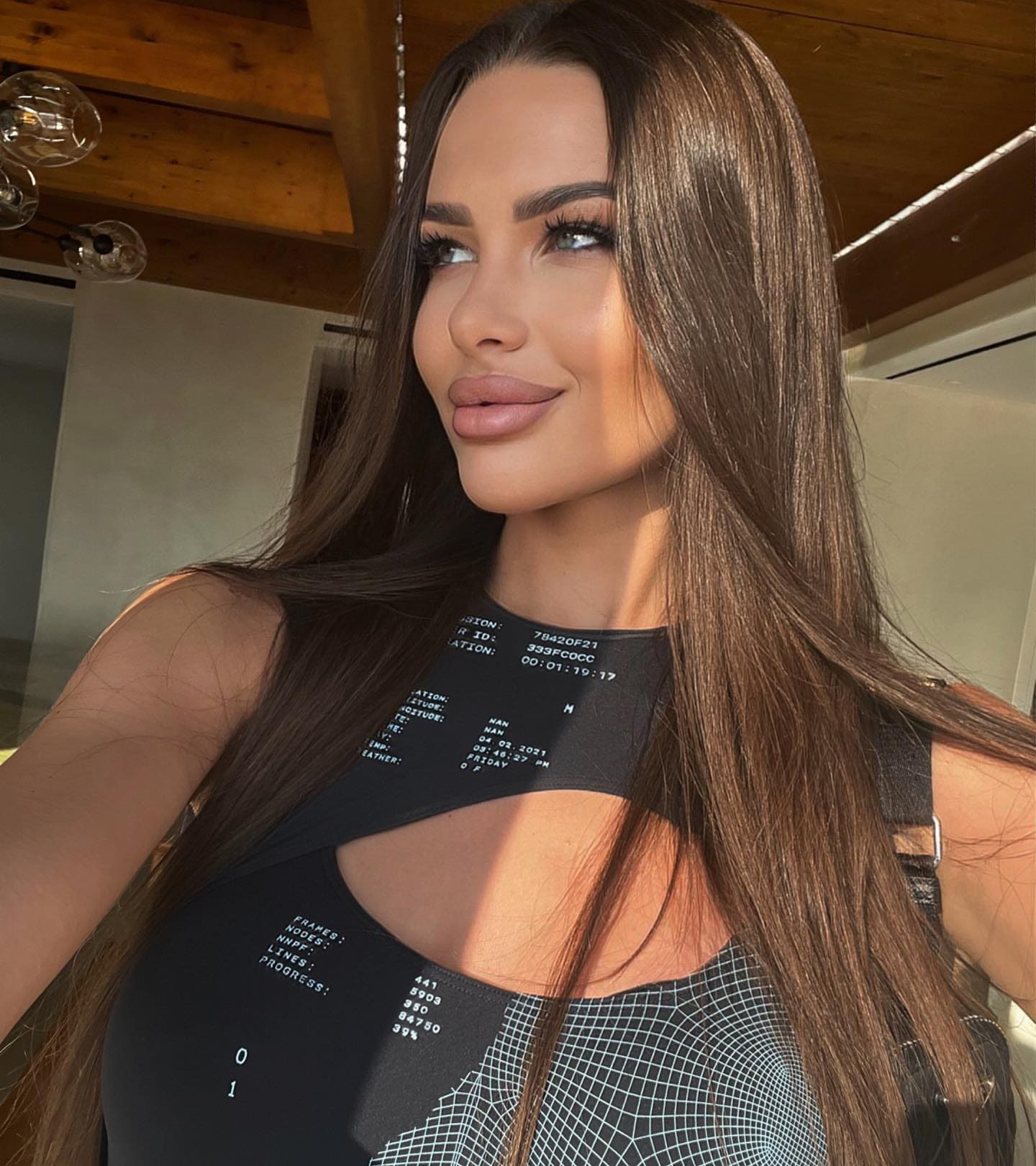 A woman with long dark hair wears a black sleeveless top with a cutout neckline, standing under a wooden ceiling.