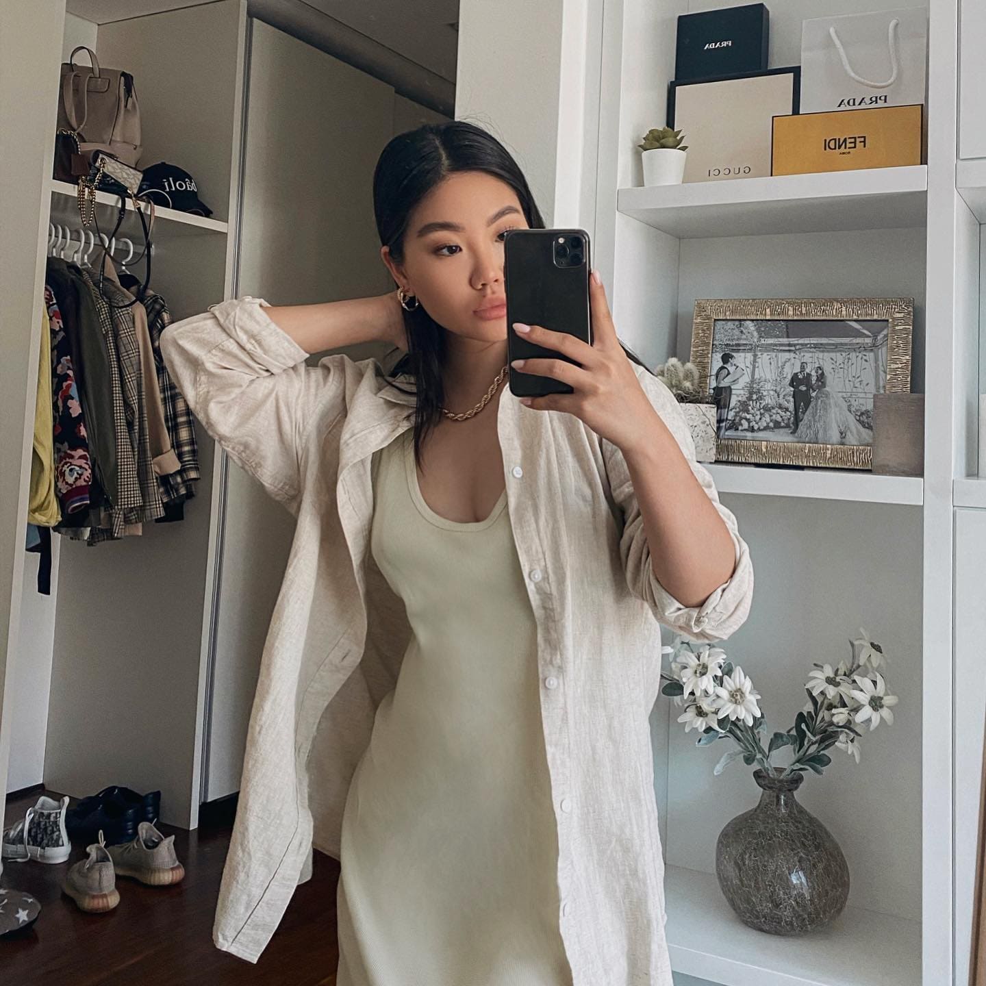 Mirror selfie in a walk-in closet showing a light slip dress under an open linen shirt, one hand behind her head.